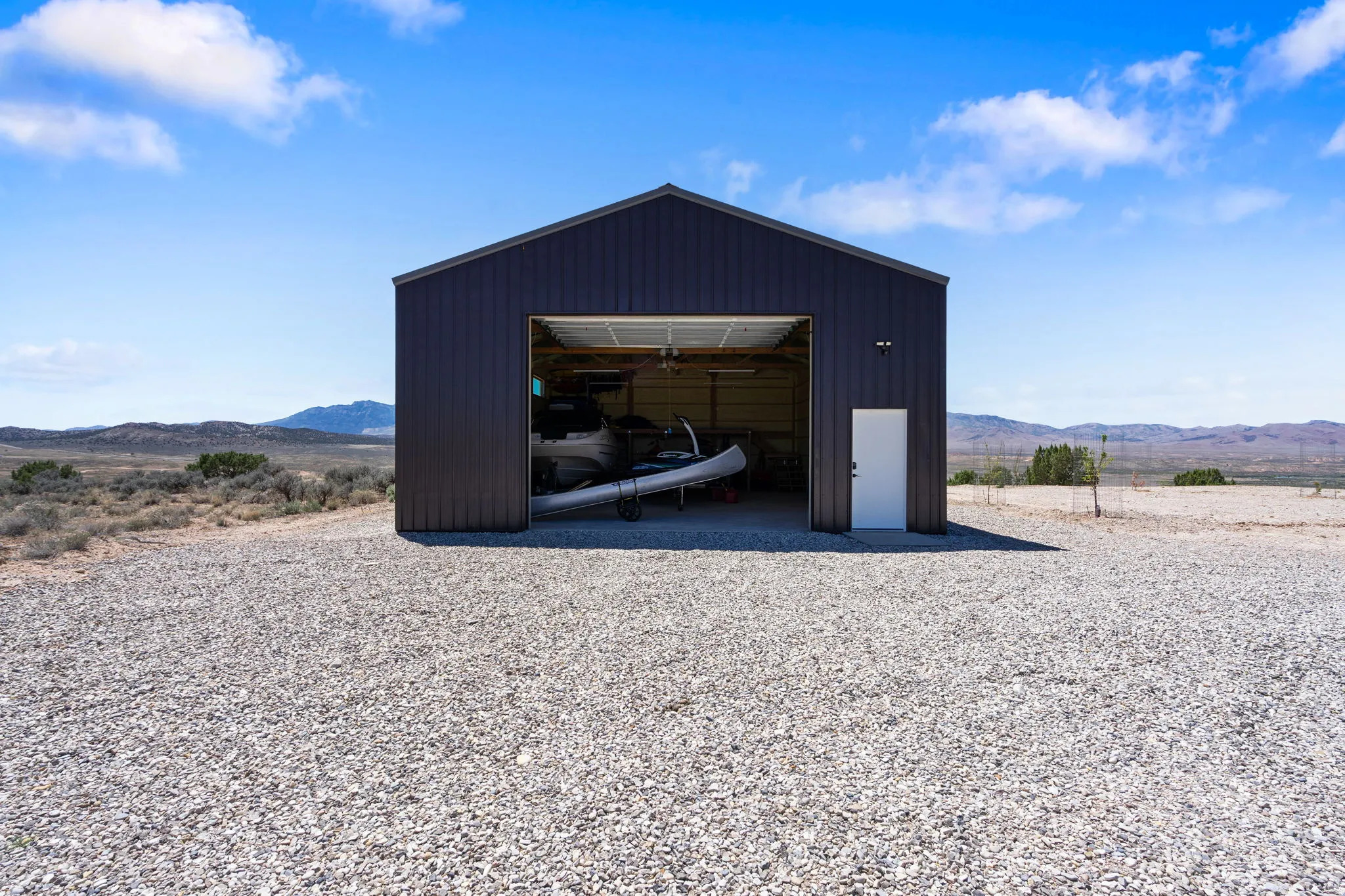 Spacious metal building featuring a large overhead door, an additional side entry door, and a gravel foreground