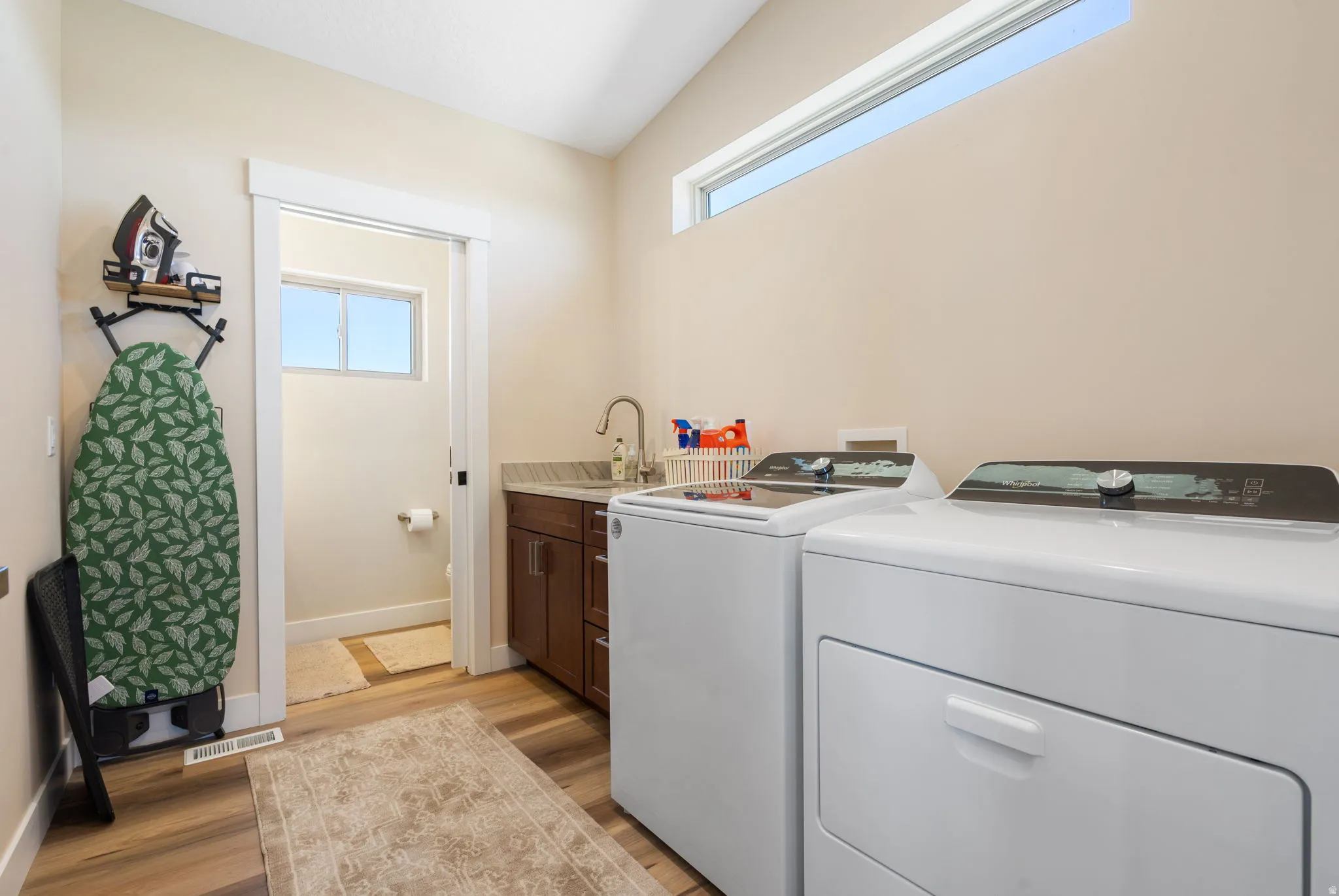 Dedicated laundry space featuring a side-by-side washer and dryer, wood-finish flooring, a built-in utility sink with a gooseneck faucet, a stone countertop, and wood cabinetry