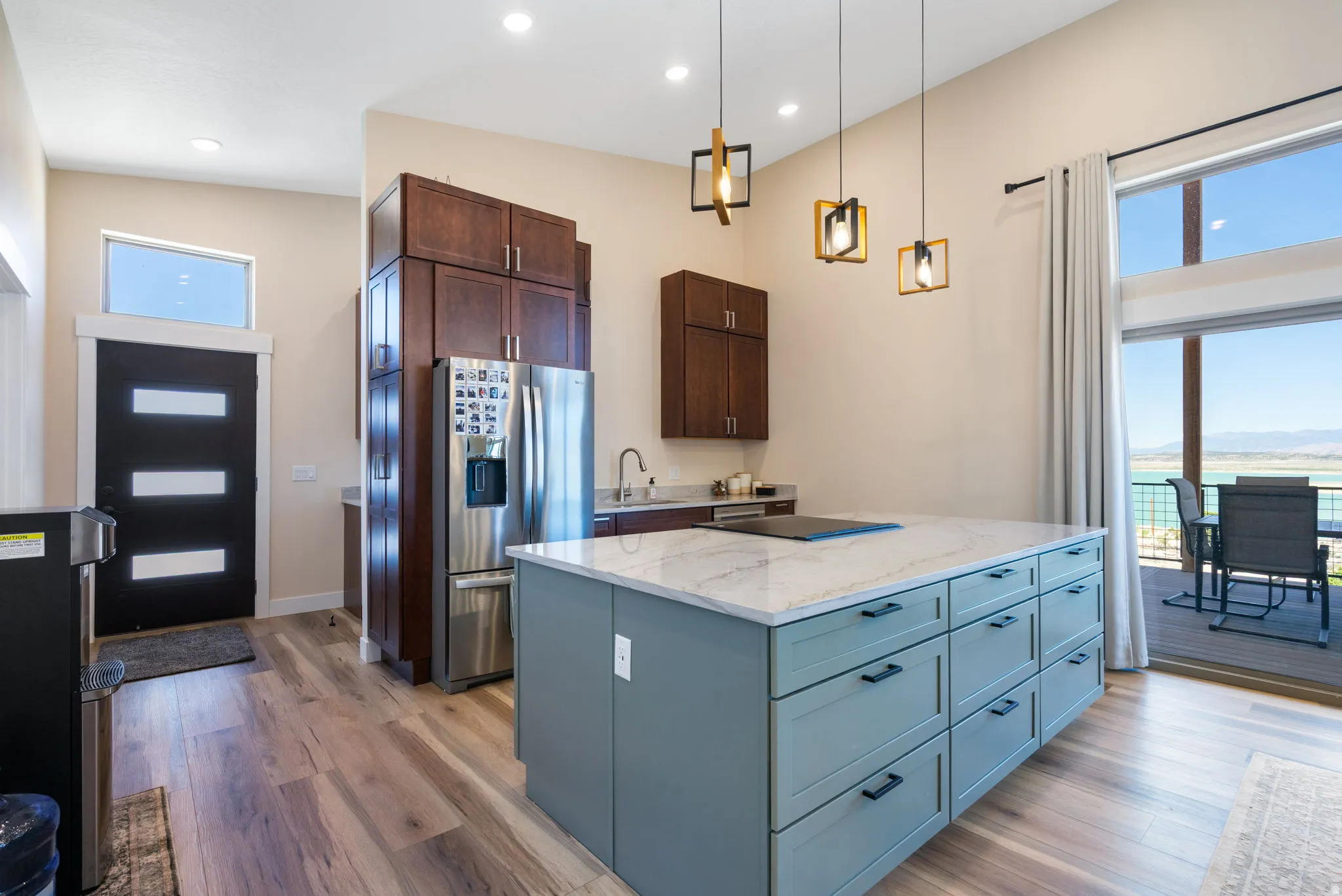 Bright kitchen featuring a substantial island with a light-colored countertop, dark wood-finish cabinetry, wood-finish flooring, and a large sliding glass door opening to an outdoor deck