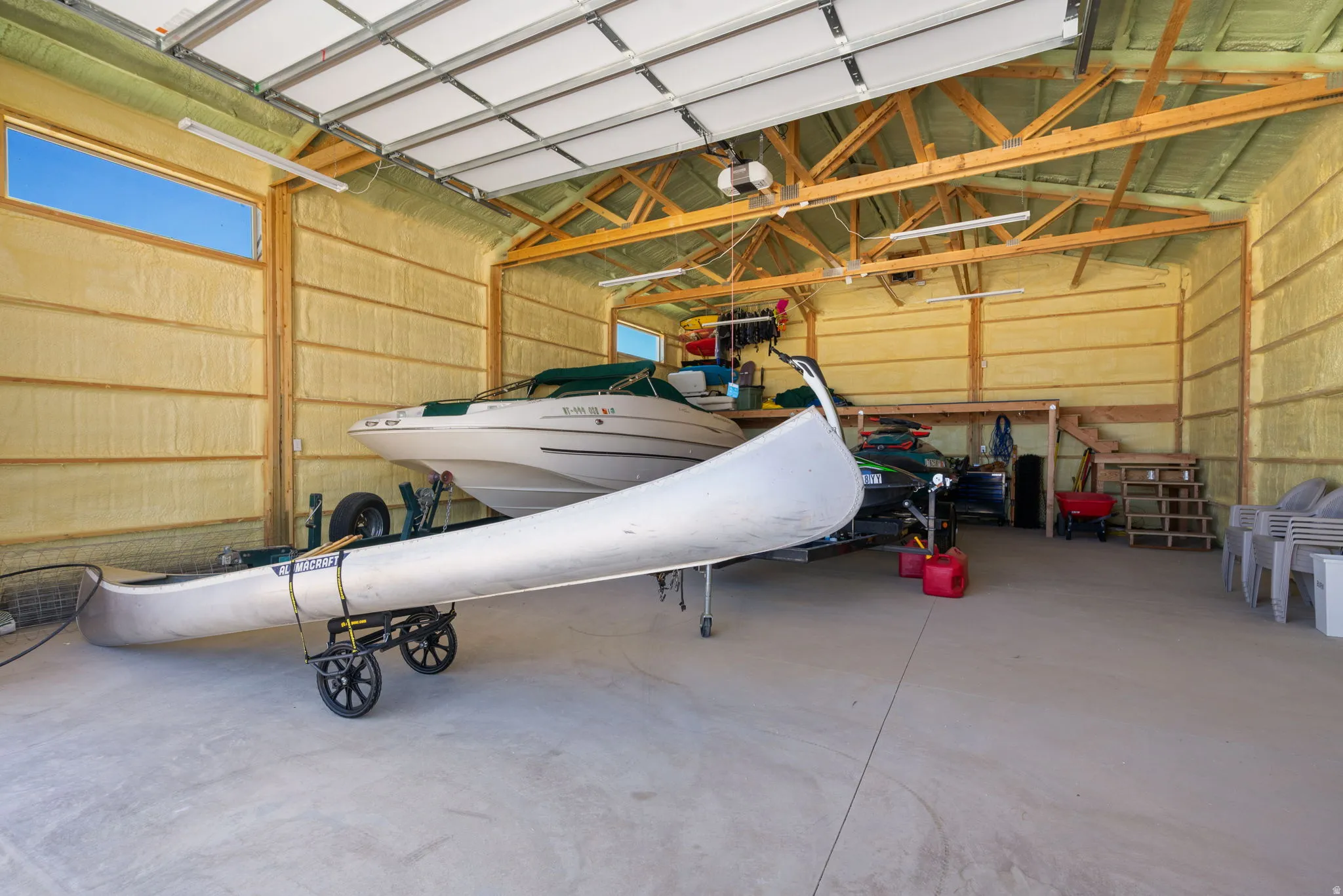 Spacious garage featuring high ceilings, exposed wood trusses, concrete flooring, and insulated walls
