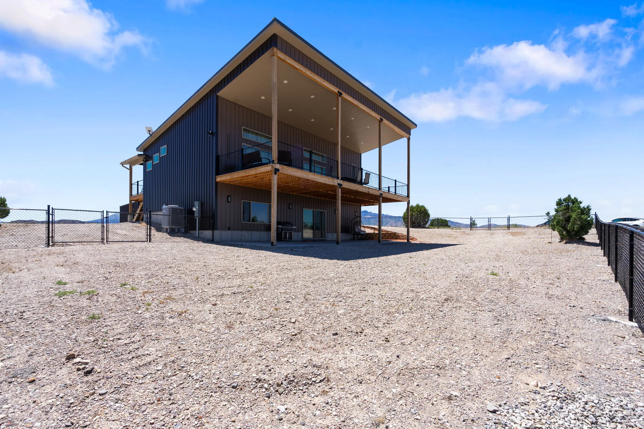 Modern two-story residence featuring a dark metal exterior, an upper-level covered balcony with dark railing, a lower-level covered patio, and large windows