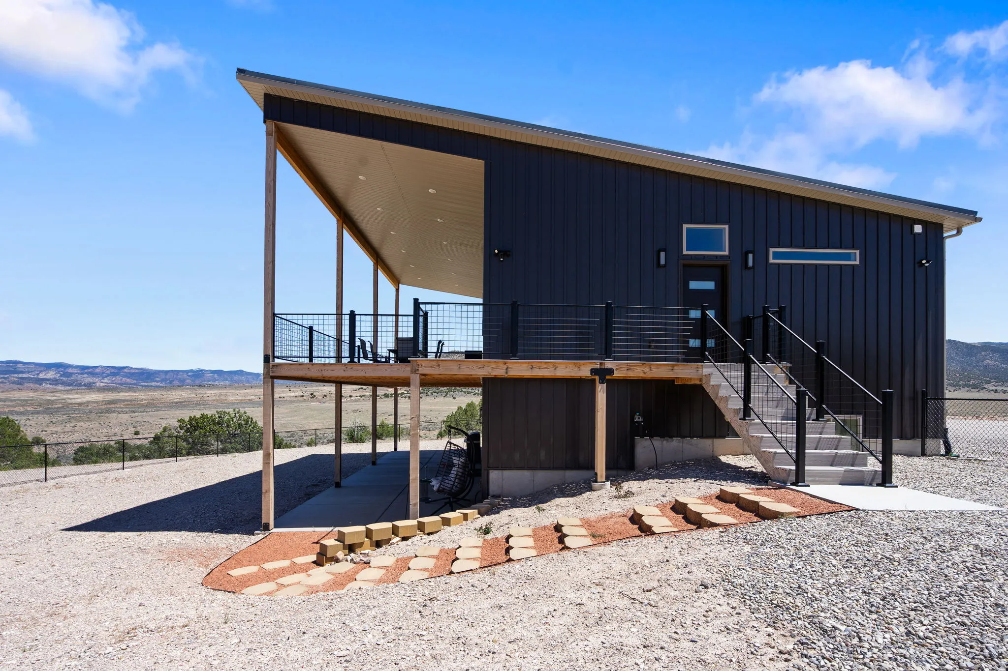 Modern exterior featuring dark vertical siding, an expansive covered porch, a concrete staircase with black railings, and a sloped roofline