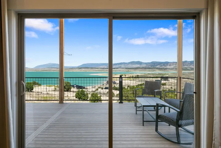 Sliding glass doors opening to an outdoor deck with metal railing overlooking a body of water and distant mountains