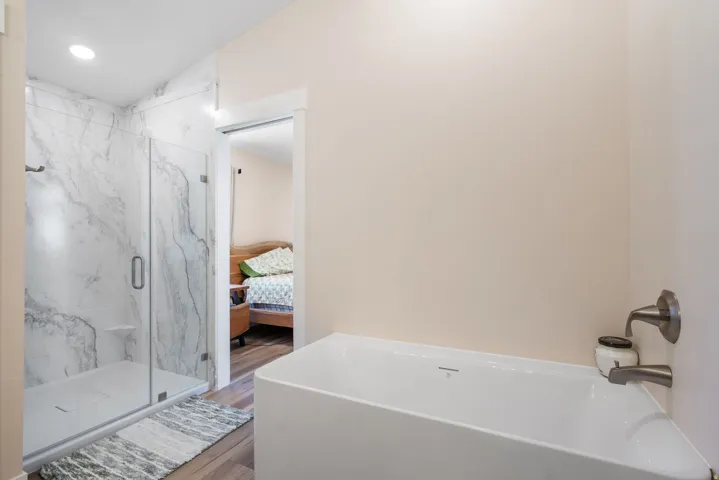 Freestanding soaking tub with brushed nickel fixtures complemented by a glass-enclosed shower featuring large format marble-look tile and a recessed light
