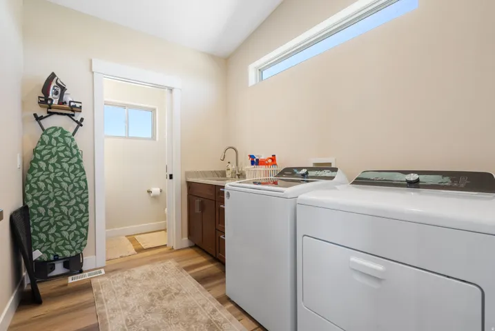 Dedicated laundry space featuring a side-by-side washer and dryer, wood-finish flooring, a built-in utility sink with a gooseneck faucet, a stone countertop, and wood cabinetry