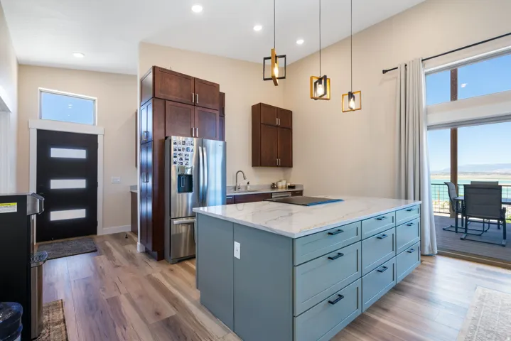 Bright kitchen featuring a substantial island with a light-colored countertop, dark wood-finish cabinetry, wood-finish flooring, and a large sliding glass door opening to an outdoor deck
