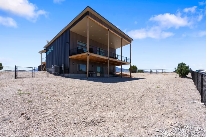 Modern two-story residence featuring a dark metal exterior, an upper-level covered balcony with dark railing, a lower-level covered patio, and large windows