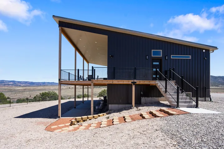 Modern exterior featuring dark vertical siding, an expansive covered porch, a concrete staircase with black railings, and a sloped roofline