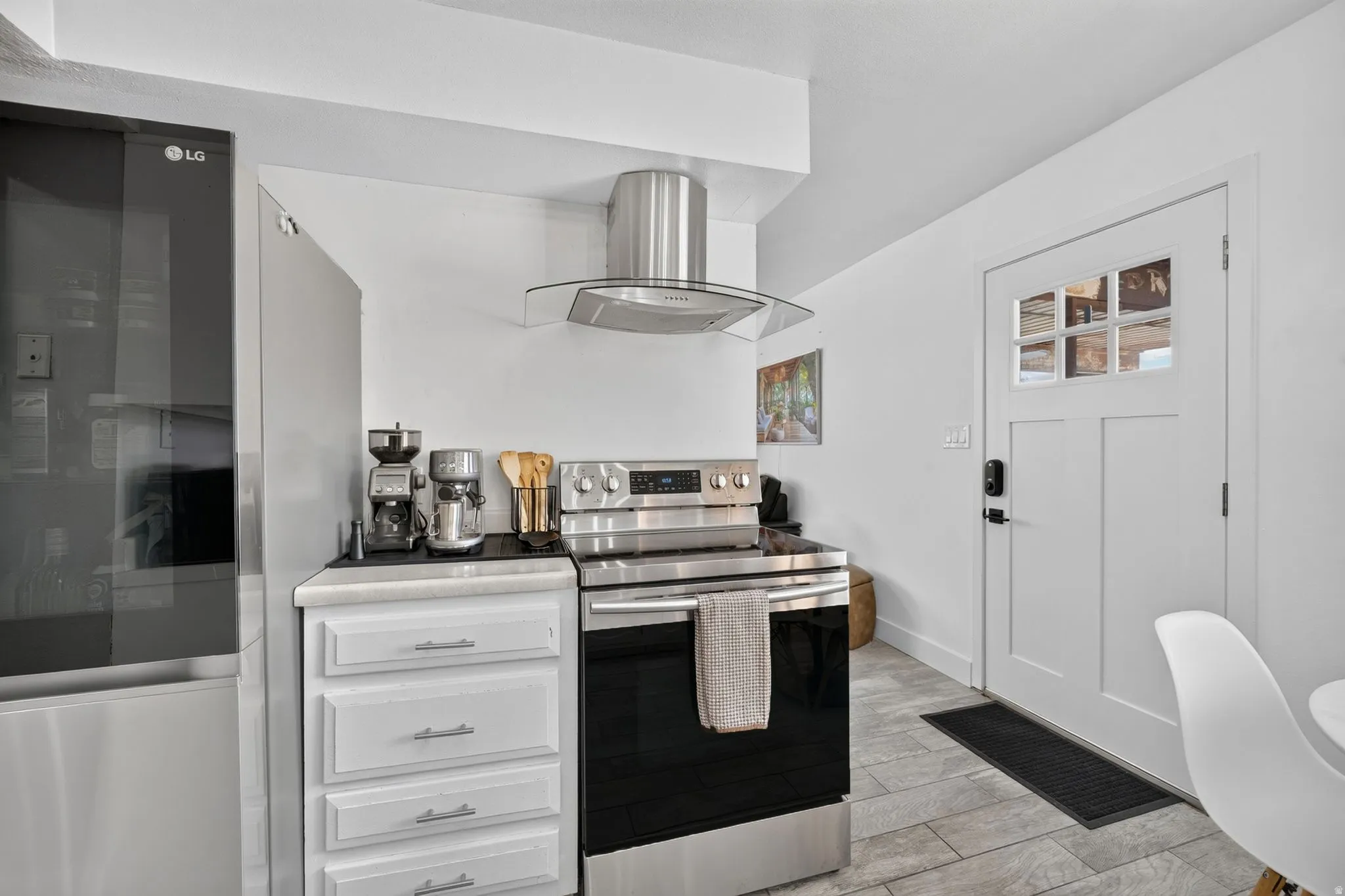 Kitchen area featuring stainless steel appliances, a range with an overhead vent hood, white cabinetry with silver hardware, and light-toned flooring