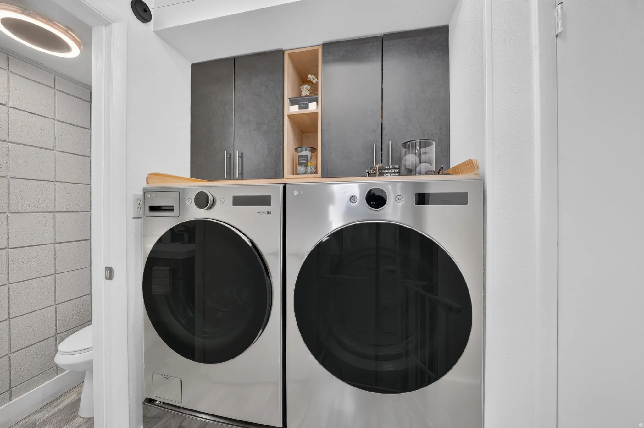 Dedicated laundry area featuring a wood-finish countertop, dark gray cabinetry, and open shelving