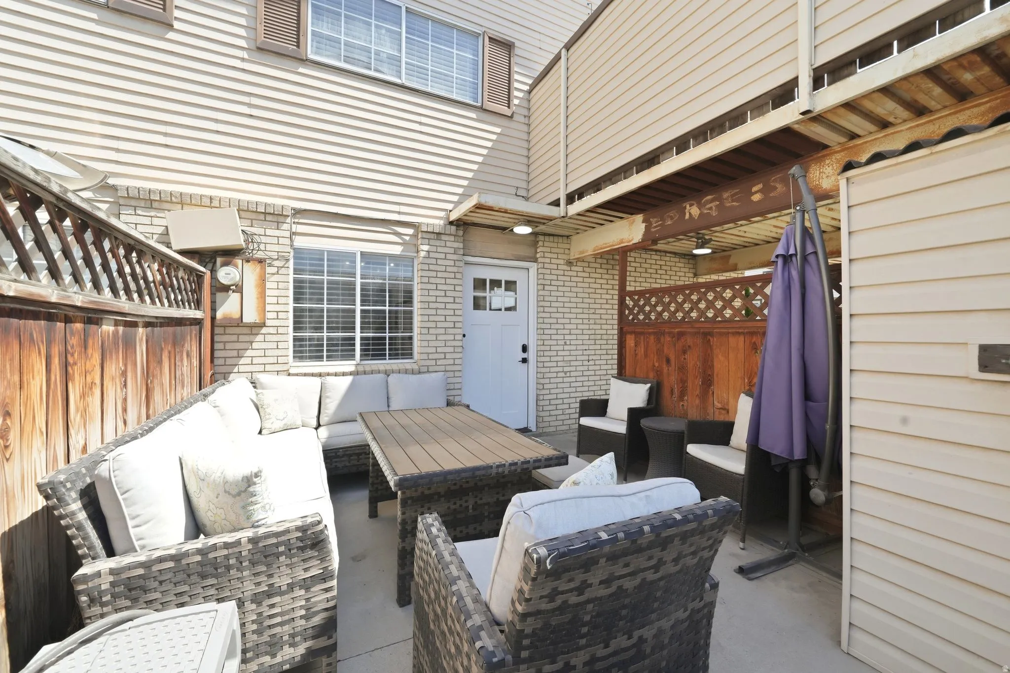 Outdoor patio space featuring a concrete slab, a wooden privacy fence, and a brick exterior wall