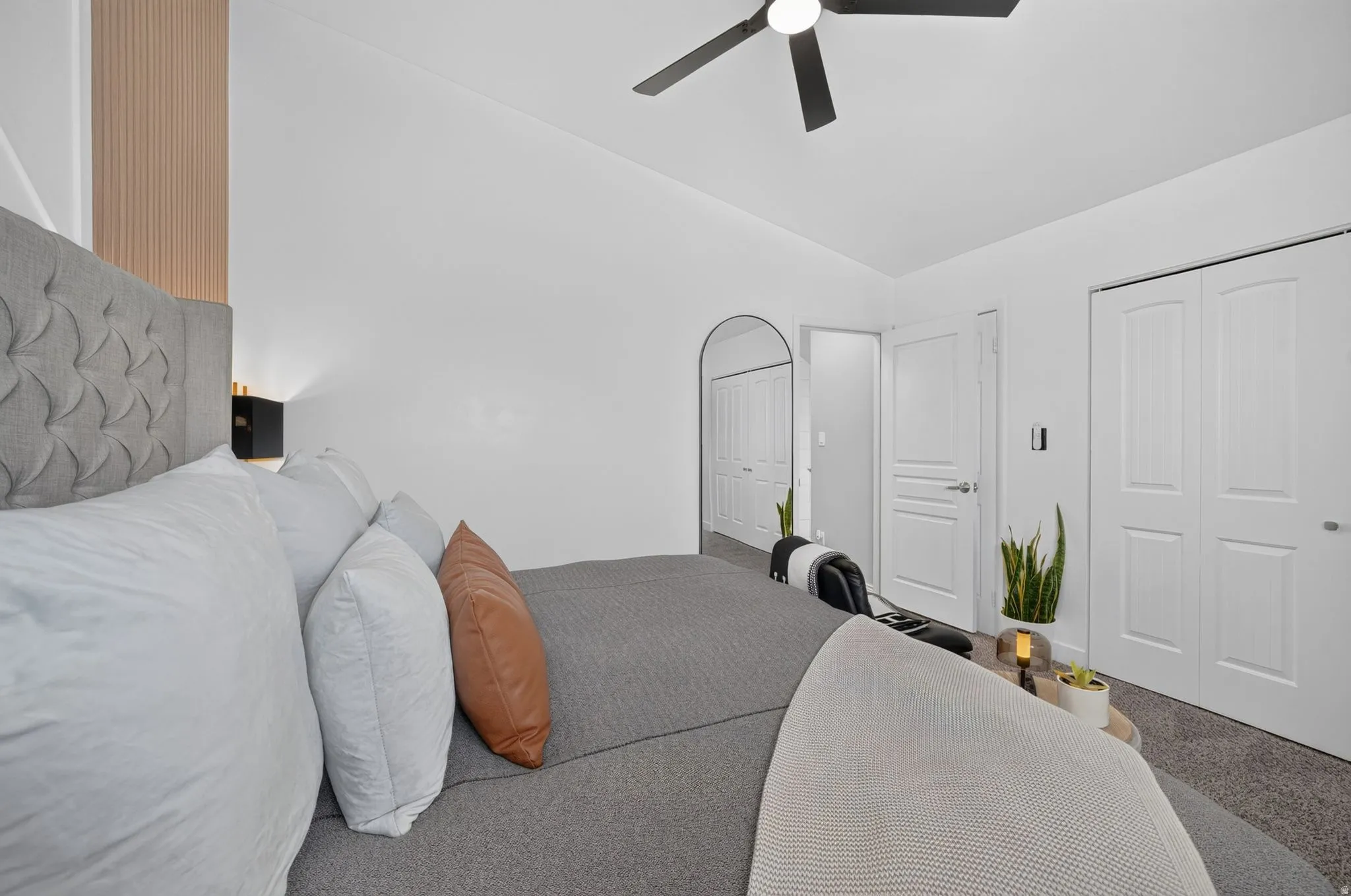 Bedroom featuring a tufted fabric headboard, a ceiling fan, and light-colored carpeting