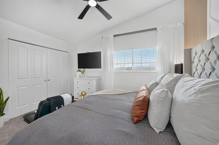 Vaulted ceilings featuring a ceiling fan, white bi-fold closet doors, and large windows with horizontal blinds
