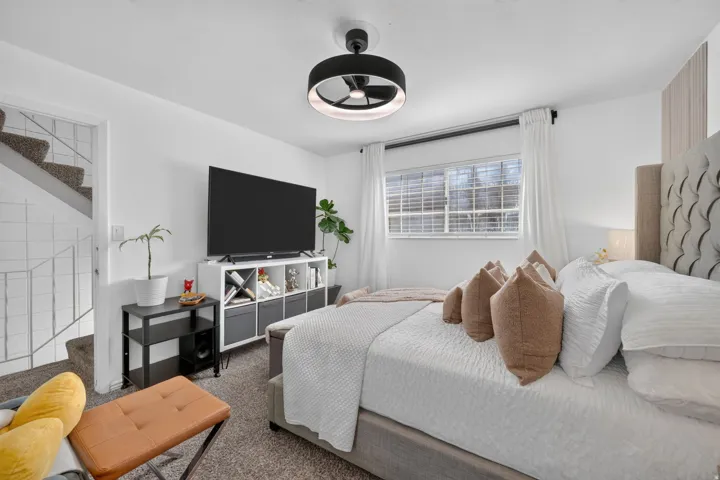 Carpeted bedroom with a modern ceiling light fixture, white walls, and a window featuring white blinds