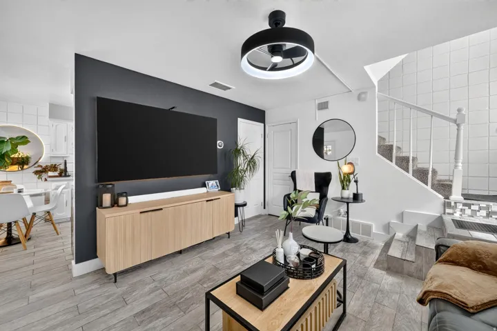 Living area featuring a dark accent wall with a wall-mounted television, light wood-finish media console, and light wood-finish flooring