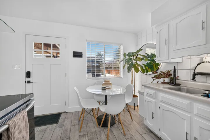White kitchen featuring wood-finish flooring, white cabinetry, integrated sink, and white tile backsplash