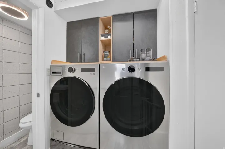 Dedicated laundry area featuring a wood-finish countertop, dark gray cabinetry, and open shelving