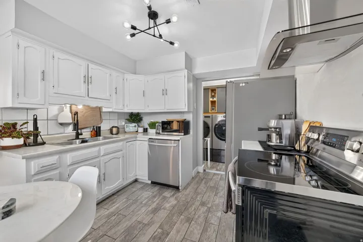 Kitchen featuring white cabinetry, wood-finish flooring, stainless steel appliances, and a contemporary light fixture