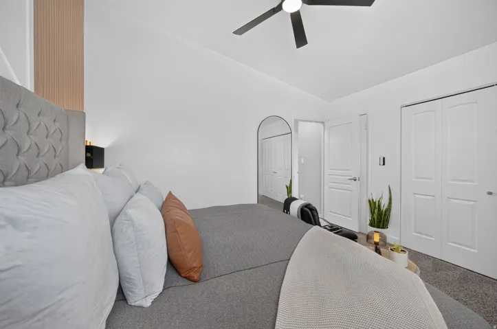Bedroom featuring a tufted fabric headboard, a ceiling fan, and light-colored carpeting