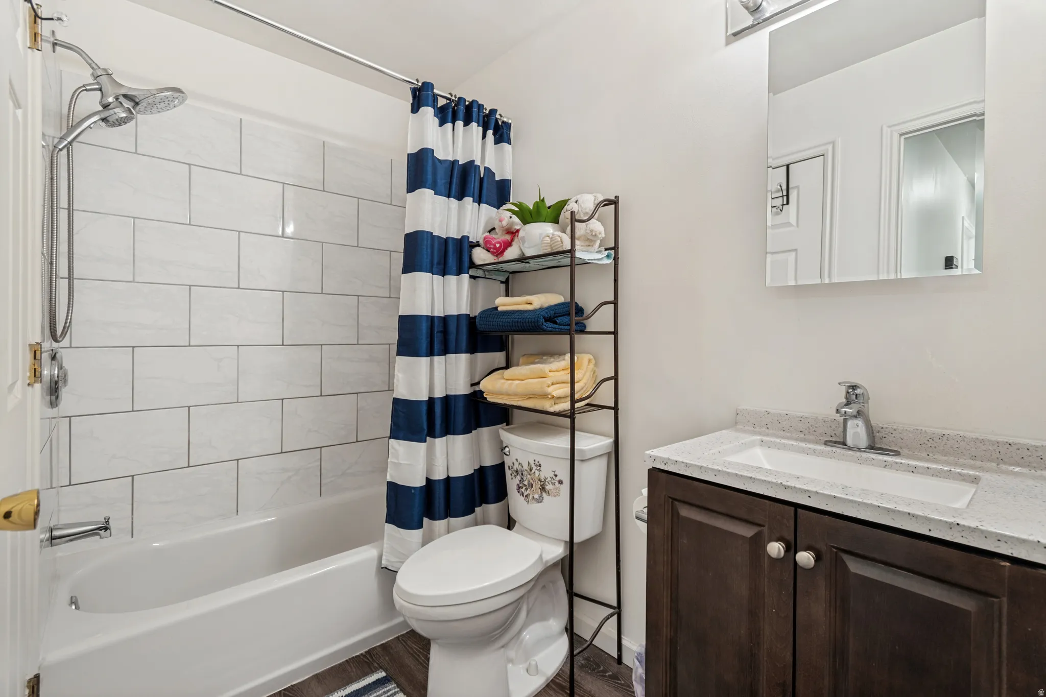 Full bathroom featuring a tub/shower combination with white subway tile surround, a dark wood-finish vanity with an integrated white sink, and a speckled countertop