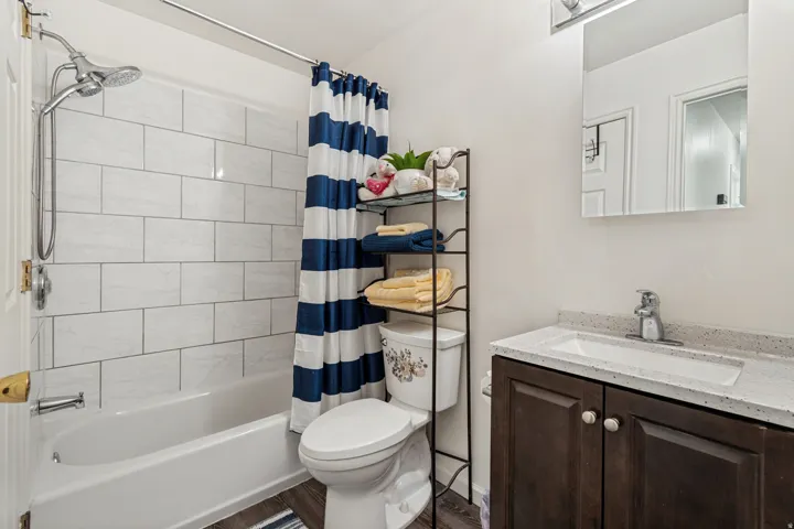 Full bathroom featuring a tub/shower combination with white subway tile surround, a dark wood-finish vanity with an integrated white sink, and a speckled countertop