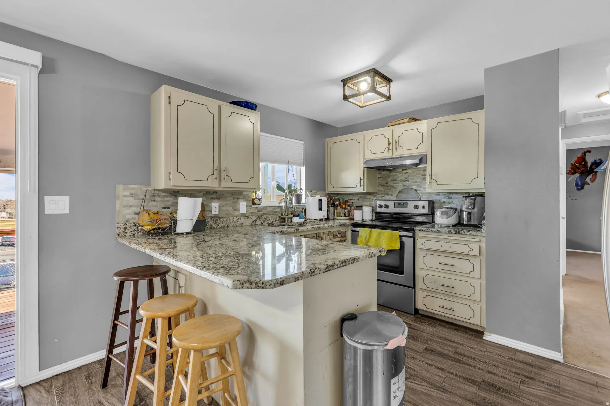 Kitchen featuring an extended peninsula with a stone-finish countertop, cream-colored cabinetry, stainless steel range, and wood-finish flooring