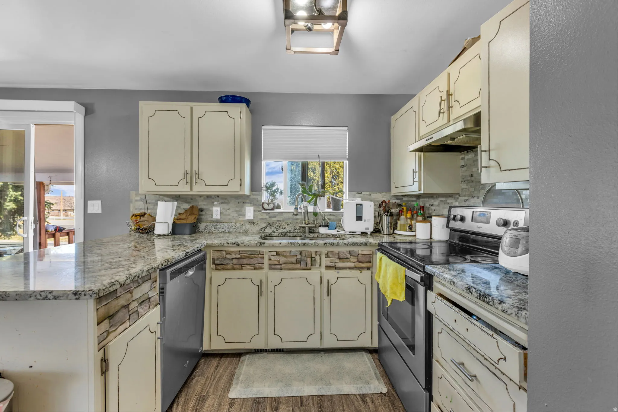 Kitchen featuring granite countertops, stone-look backsplash, wood-finish flooring, and cream cabinetry with dark hardware