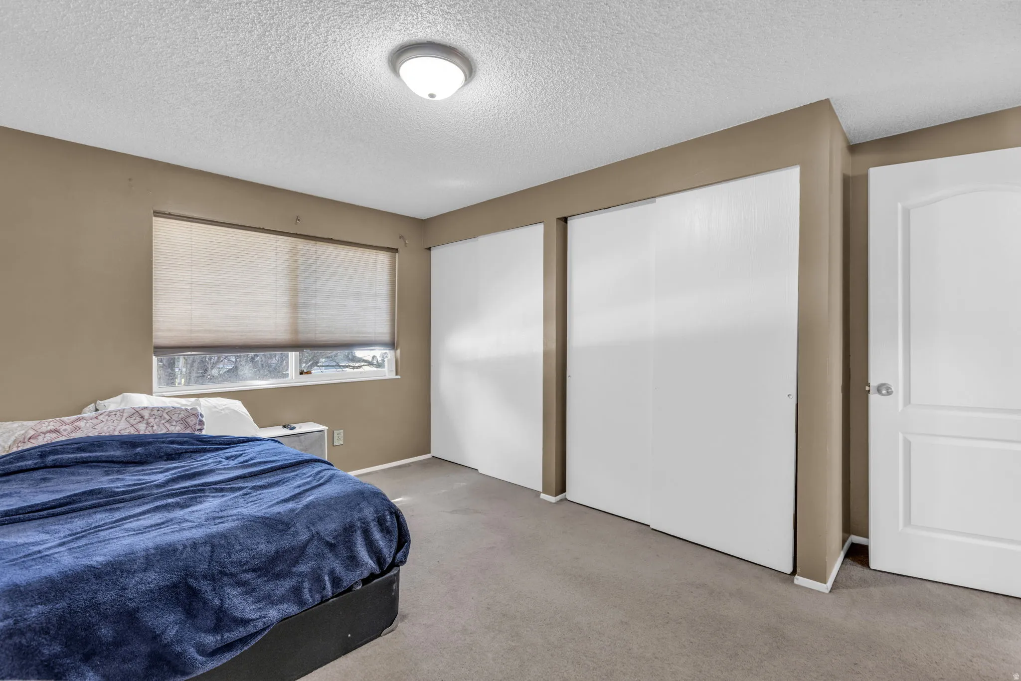 Bedroom featuring neutral-toned walls, textured ceiling, carpeted flooring, two sliding closet doors, and a paneled door