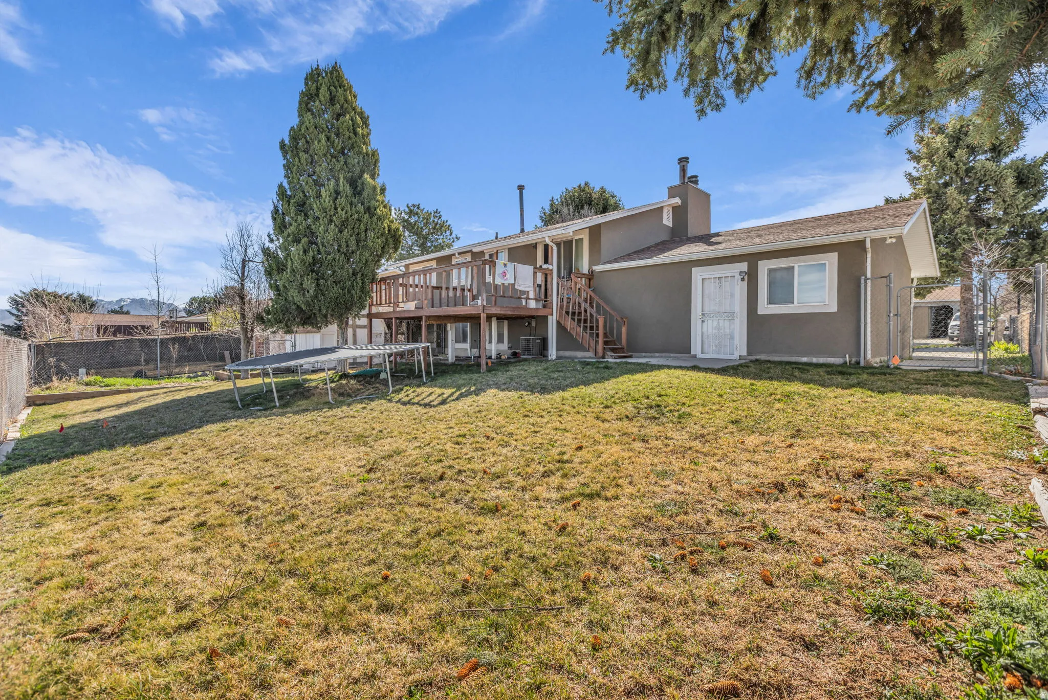 Spacious backyard featuring an elevated wood deck with stairs, a stucco exterior, and mature perimeter trees