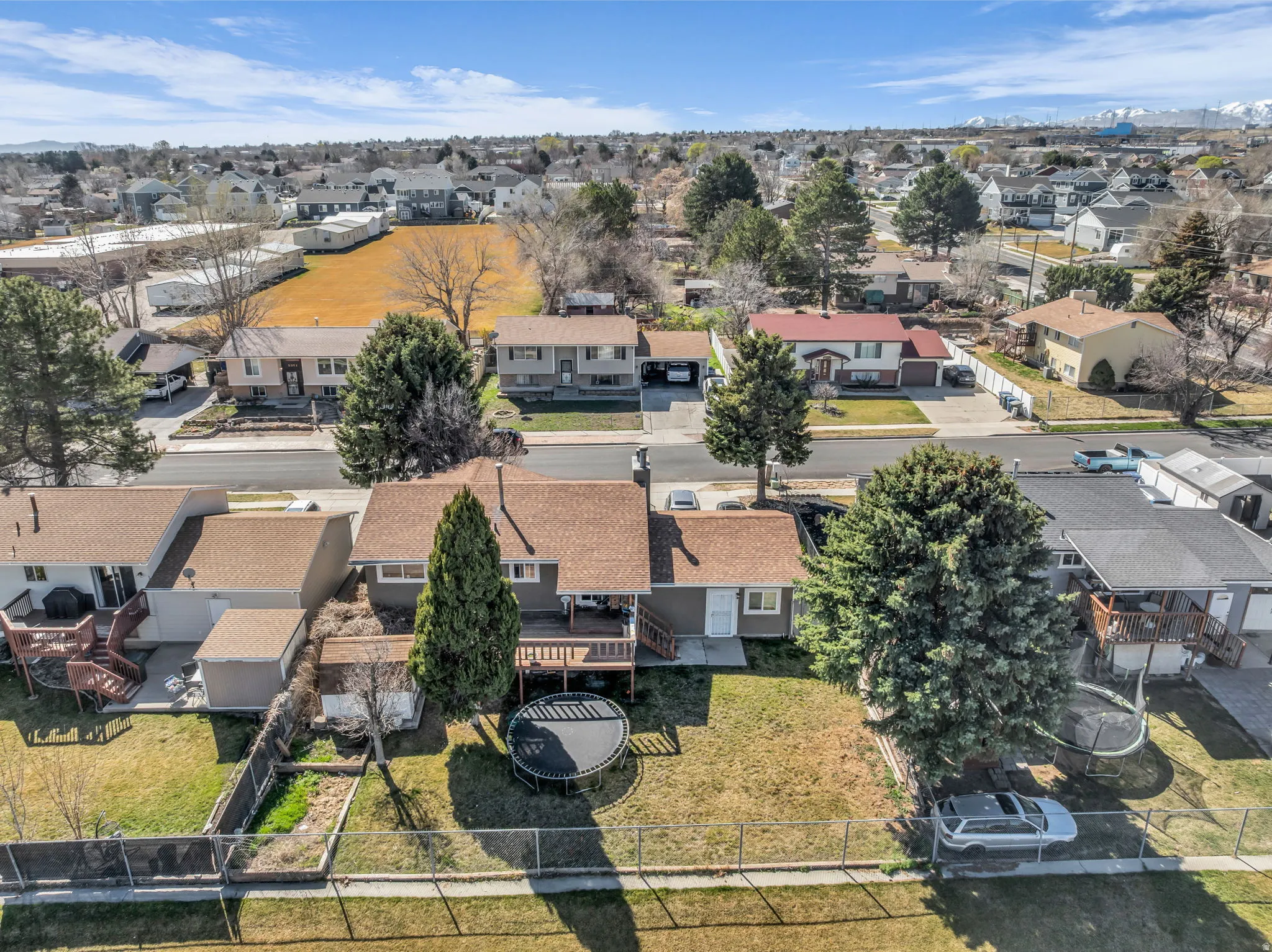 Residential property featuring an expansive backyard, mature trees, a wooden deck, and a fenced perimeter