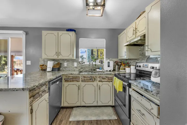 Kitchen featuring granite countertops, stone-look backsplash, wood-finish flooring, and cream cabinetry with dark hardware