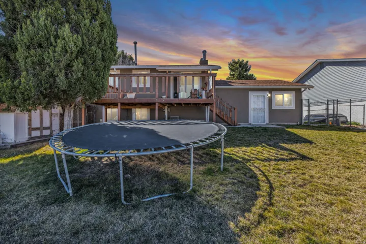 Expansive backyard featuring a brown stucco exterior, a multi-level wood deck, a rear entry door, and a mature tree