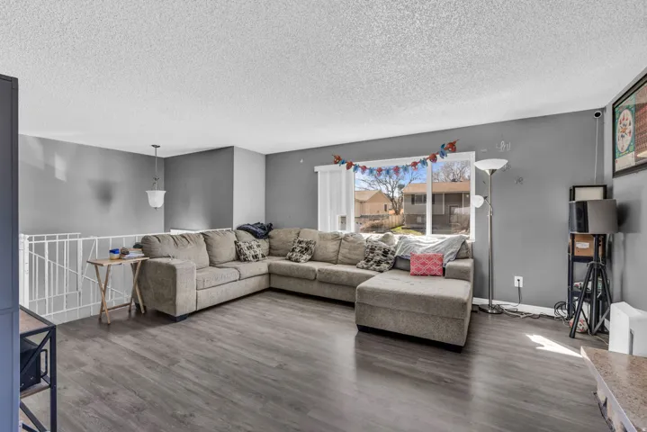 Spacious living area featuring wood-finish flooring, a large window, neutral wall tones, and a white railing