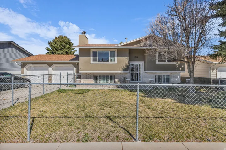 Split-level residence featuring a dual-car garage with white doors, stucco exterior, and a stone-finish foundation