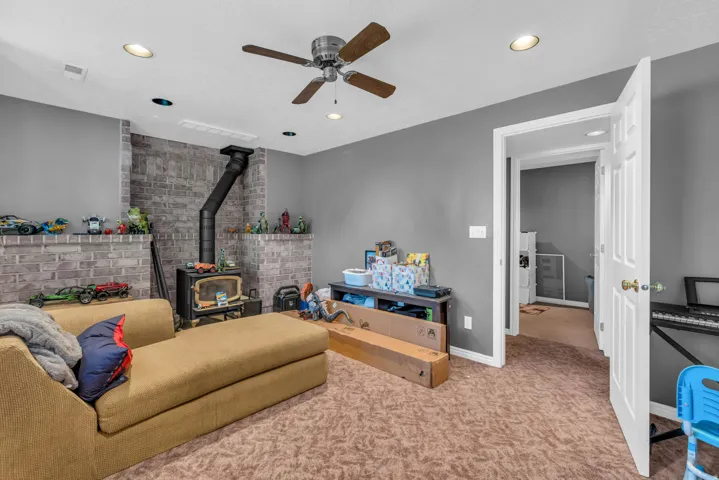 Finished room featuring a brick accent wall with a central wood-burning stove, recessed lighting, and a ceiling fan