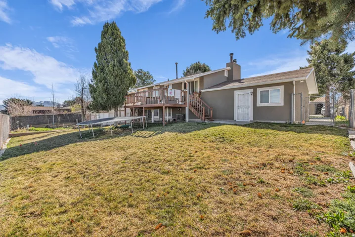 Spacious backyard featuring an elevated wood deck with stairs, a stucco exterior, and mature perimeter trees