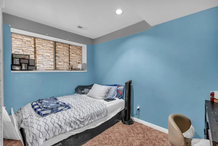 Recessed lighting illuminates a space featuring a window with stone-look blinds, light blue walls, and a light brown carpet