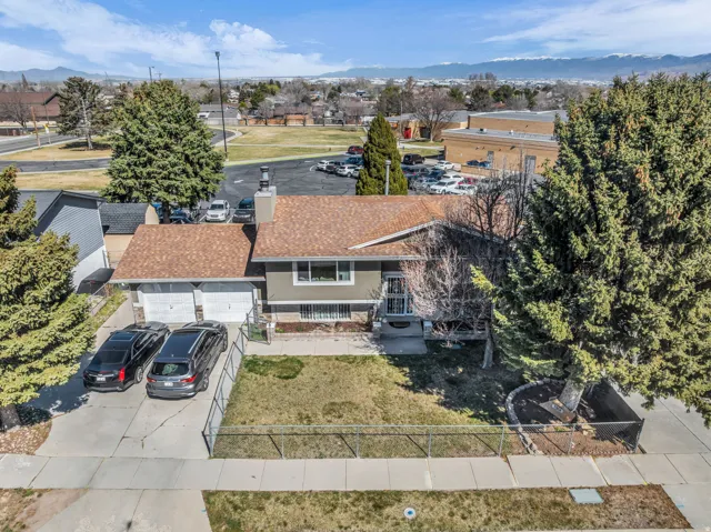 Split-level residence featuring a two-car garage, mature front yard trees, front lawn area, and a paved driveway