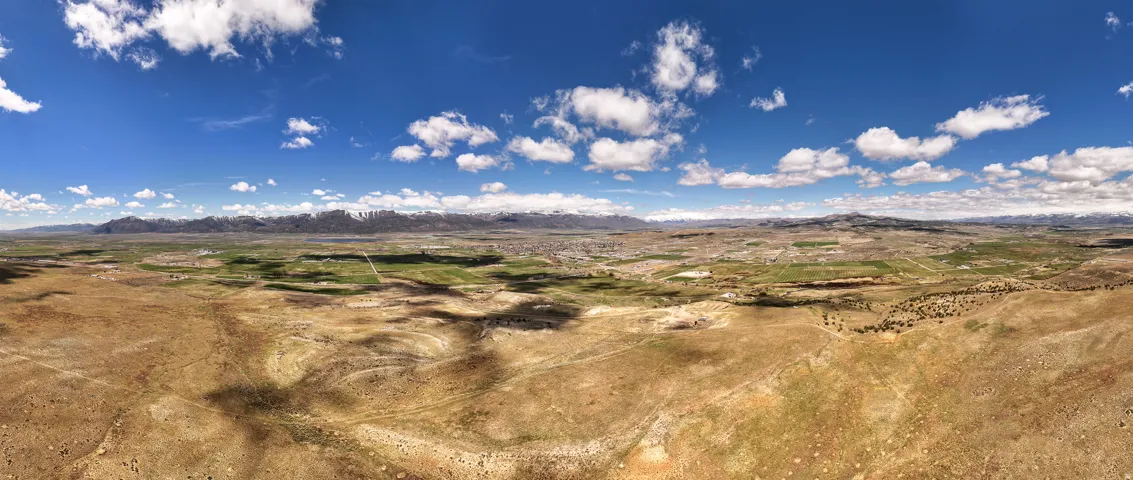Expansive desert landscape with distant mountains under a blue sky with scattered clouds