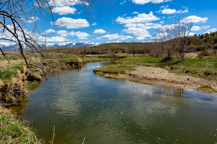 Winding river with green and tan banks under a blue sky with white clouds