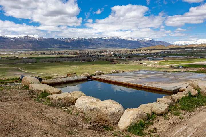 Water feature with natural stone surround and concrete basin, set against a backdrop of expansive green fields and distant snow-capped mountains