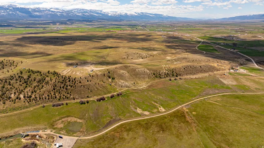 Expansive acreage featuring varied terrain, a dirt road, scattered evergreen trees, and distant snow-capped mountains