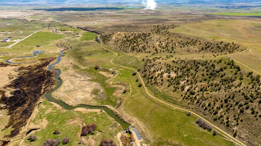 Expansive rural landscape featuring a winding river, verdant fields, a dirt road, and scattered trees