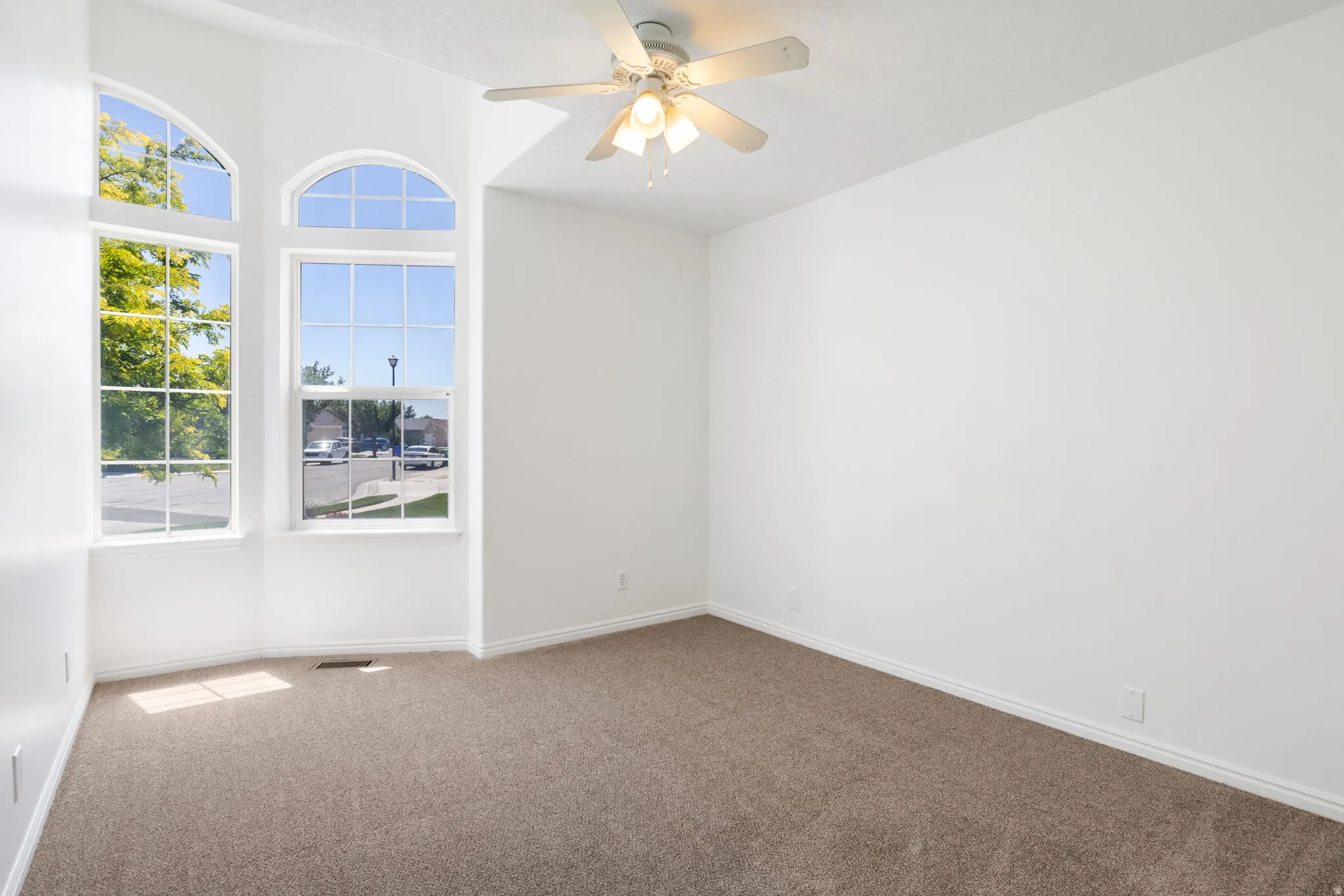 Room featuring two arched windows, a vaulted ceiling, a ceiling fan, and neutral carpet