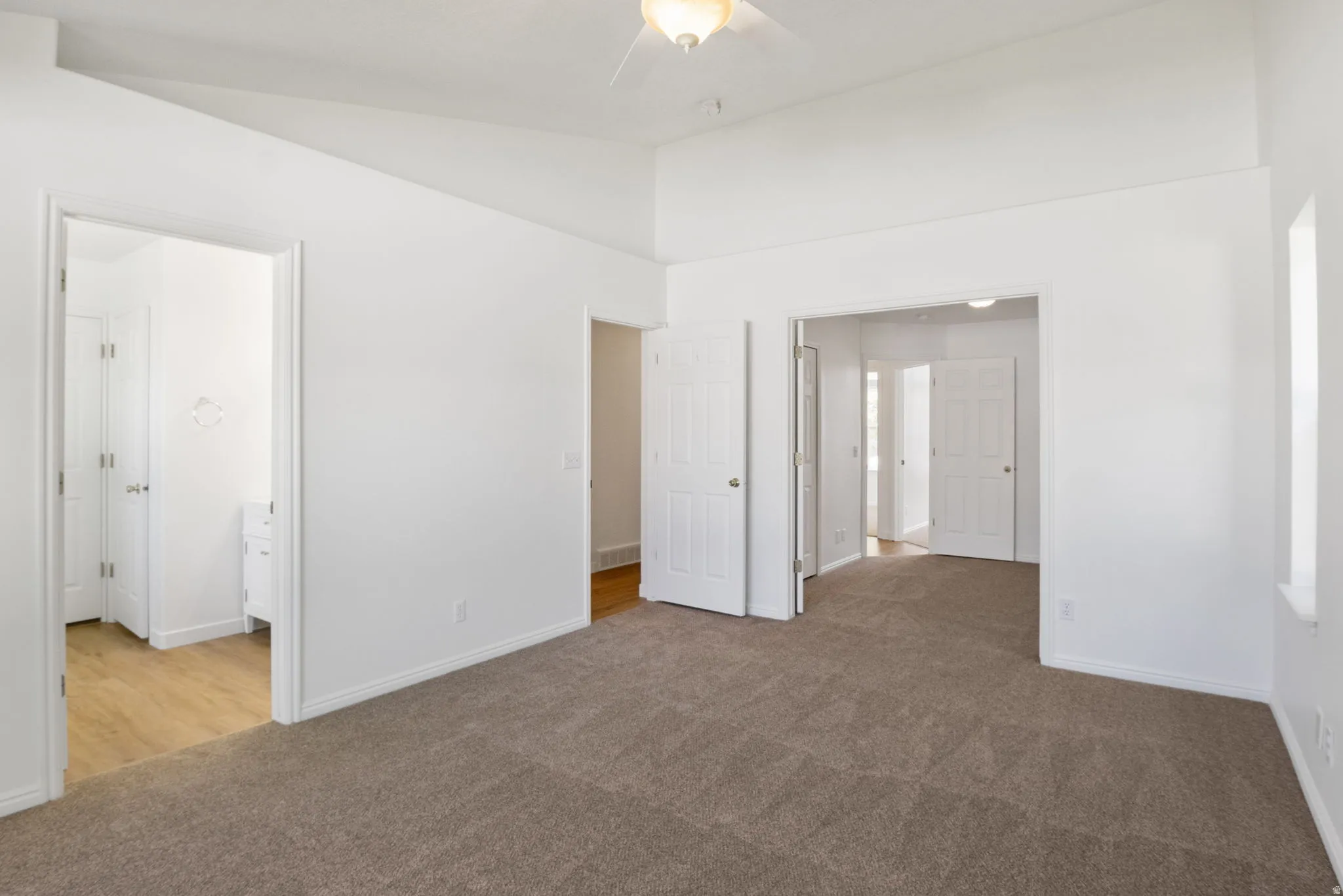 Spacious room featuring vaulted ceilings, neutral-toned carpeting, and multiple doorways