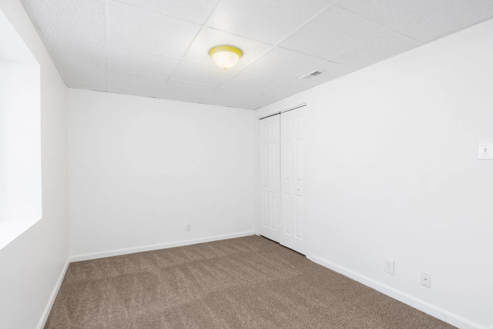 Carpeted room with white walls, a drop ceiling, and bi-fold closet doors