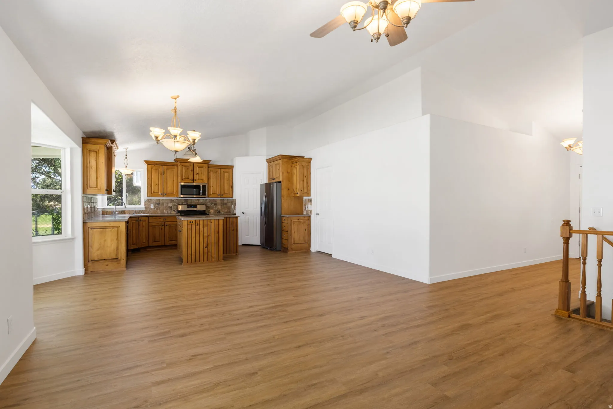 Spacious open-concept living area featuring wood-finish flooring, vaulted ceilings, and a kitchen with wood cabinetry, stainless steel appliances, and a tiled backsplash