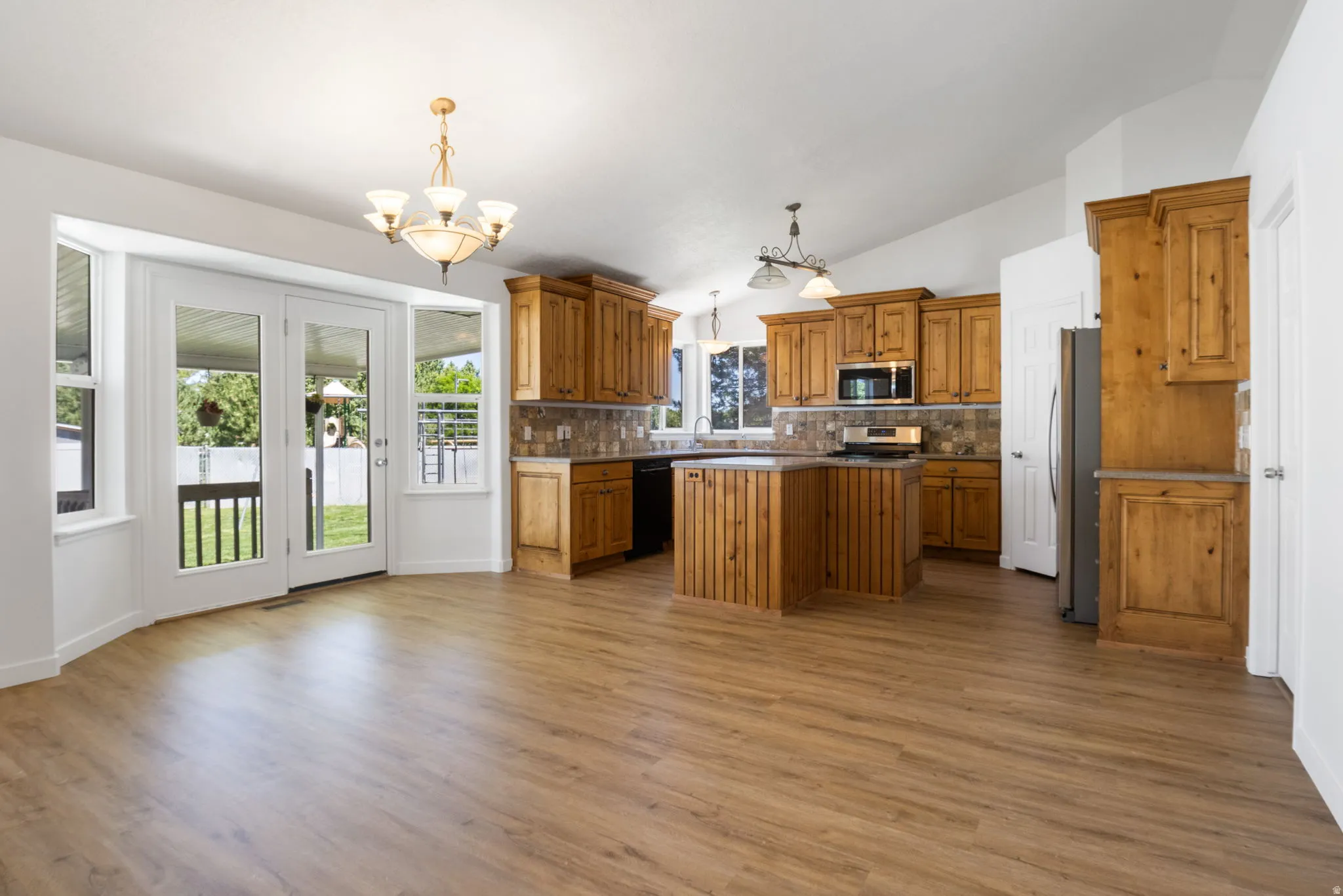 Kitchen and dining area featuring wood-finish flooring, light wood cabinetry, a tile backsplash, stainless steel appliances, and French doors opening to the exterior