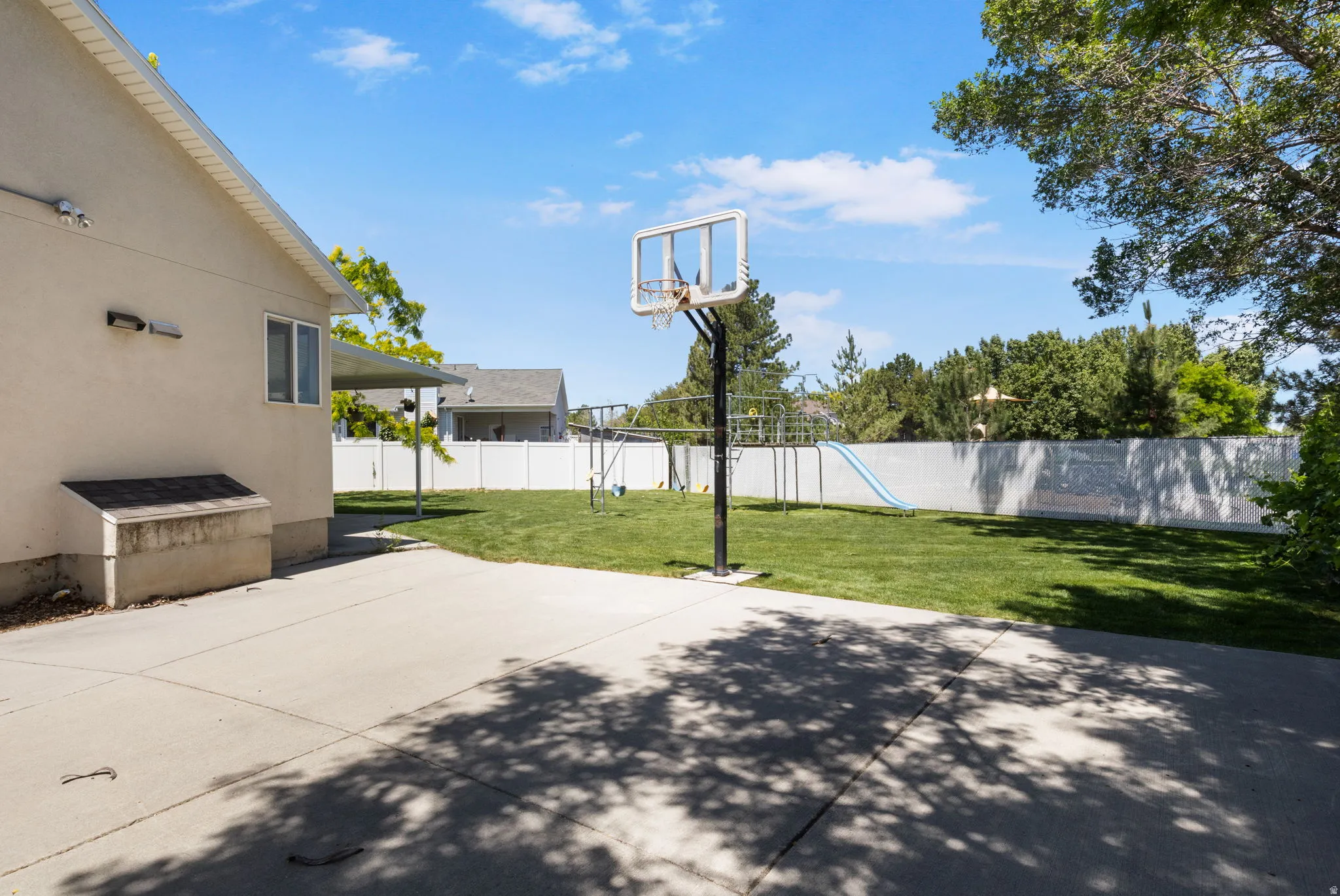 Spacious backyard featuring a concrete patio, a basketball hoop, and a manicured lawn