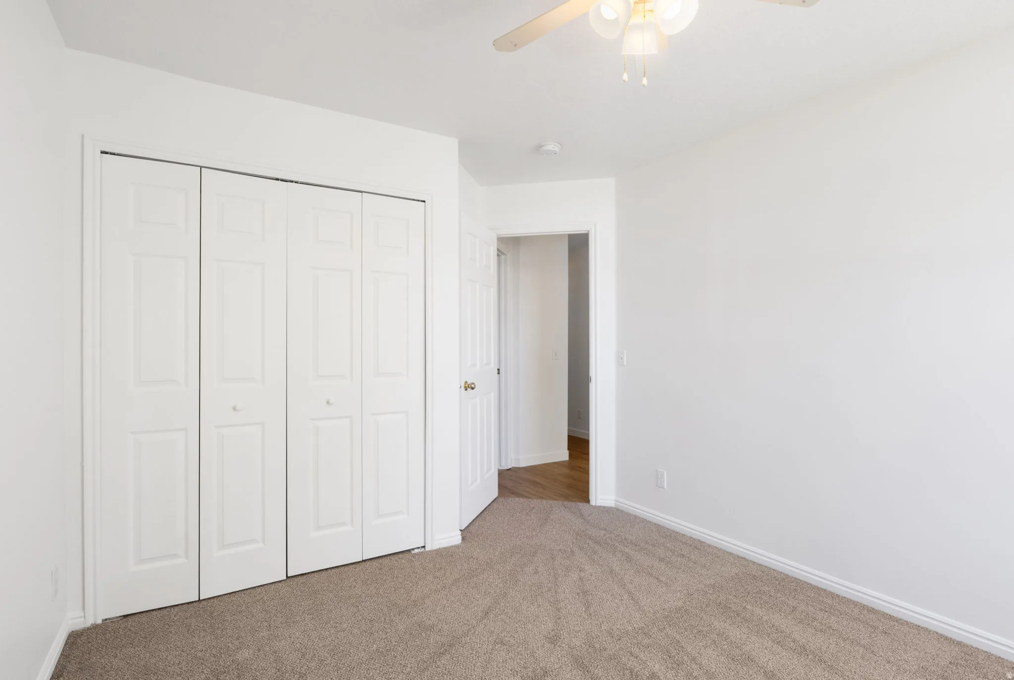 Carpeted room featuring a ceiling fan with light fixture, bifold closet doors, and white baseboards